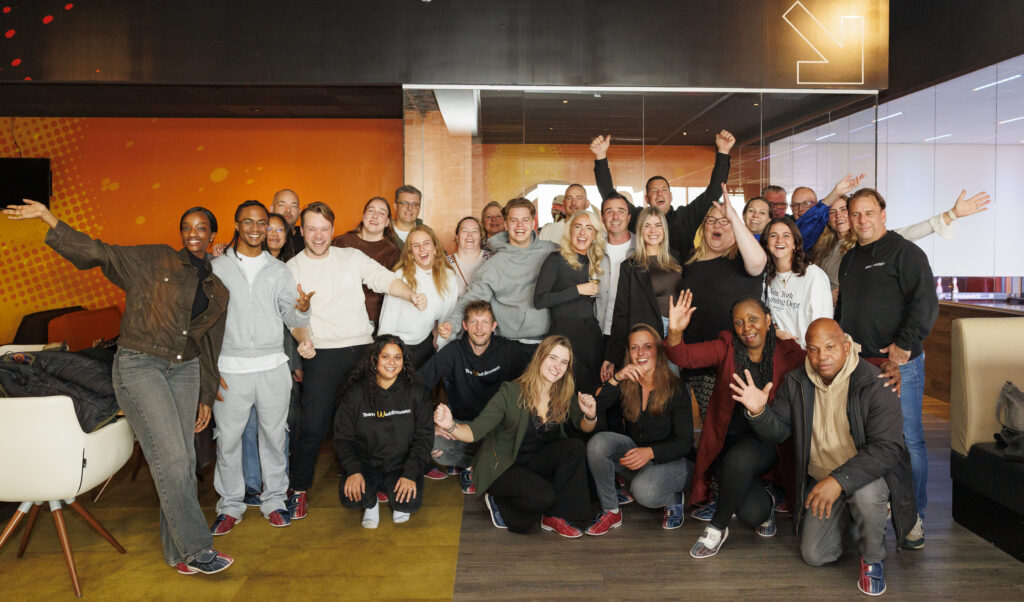 Groepsfoto van het team van Opleidingscentrum Westpoort, lachend en poserend in een kleurrijke ruimte, klaar voor het nieuwe jaar.