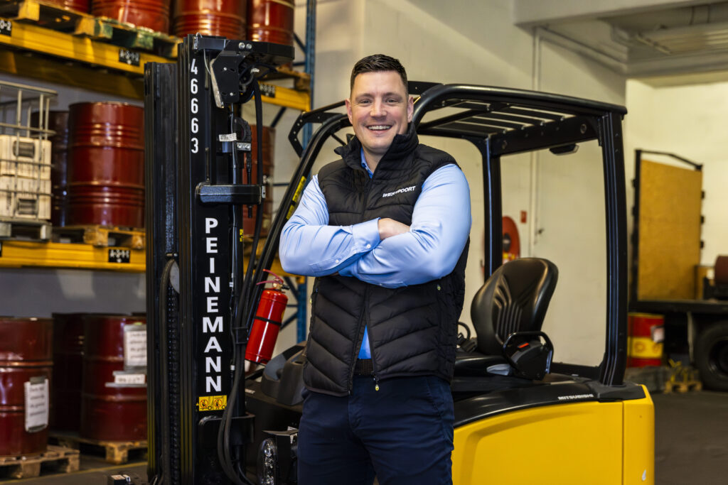 Mark Hoogweg, directeur van Opleidingscentrum Westpoort, staat lachend voor een heftruck in de loods van Westpoort in Amsterdam.