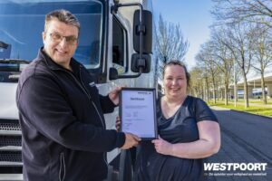 Cursist ontvangt certificaat voor Smart Tacho 2 training bij Westpoort naast vrachtwagen.